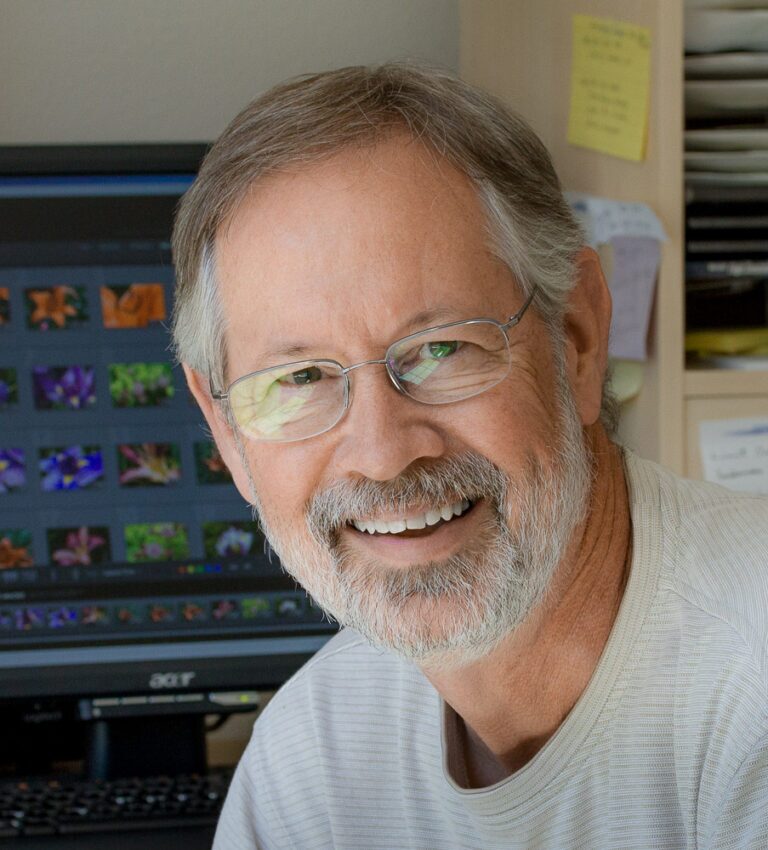 Smiling man with glasses, near computer.